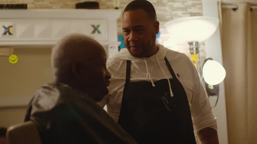 A barber chats with a client while shaving his head