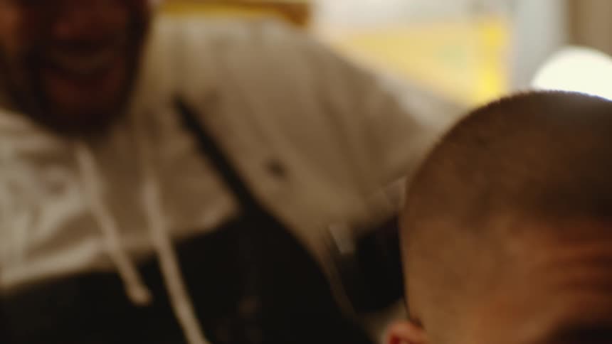 A barber laughs as a shaves a mans head