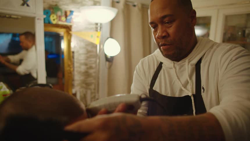 A barber is giving a man a trim with hair clippers