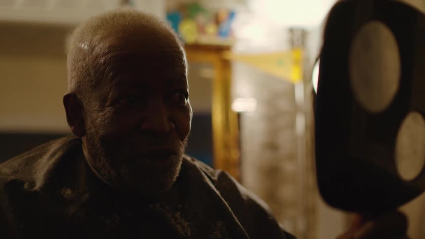 Elderly man admiring his haircut on a hand mirror inside a barber shop