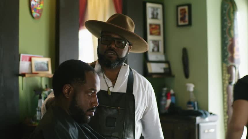 Barber wearing a hat combs the hair of a client sitting on a barber shop chair