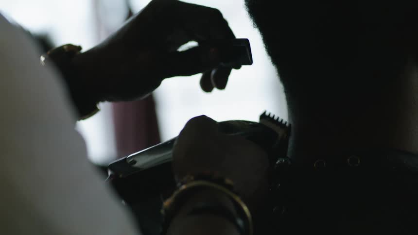 Barber with white shirt and wristwatch cuts and trims mans hair in barber shop