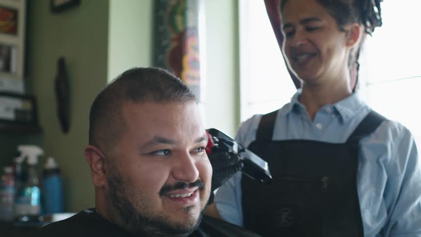Barber gives a haircut to a client with an electric shaver inside a barber shop