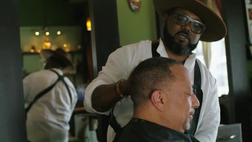 A male barber brushes the loose hair off of a clients head