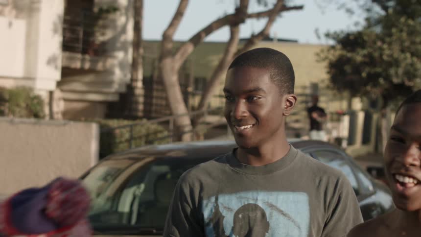 A group of young men smile and laugh next to a car