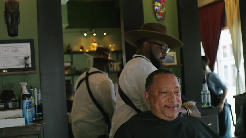 Barber brushes the head of a client to show his haircut on a hand mirror