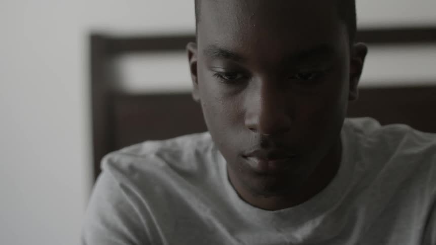 A boy looks down while sitting on a bed