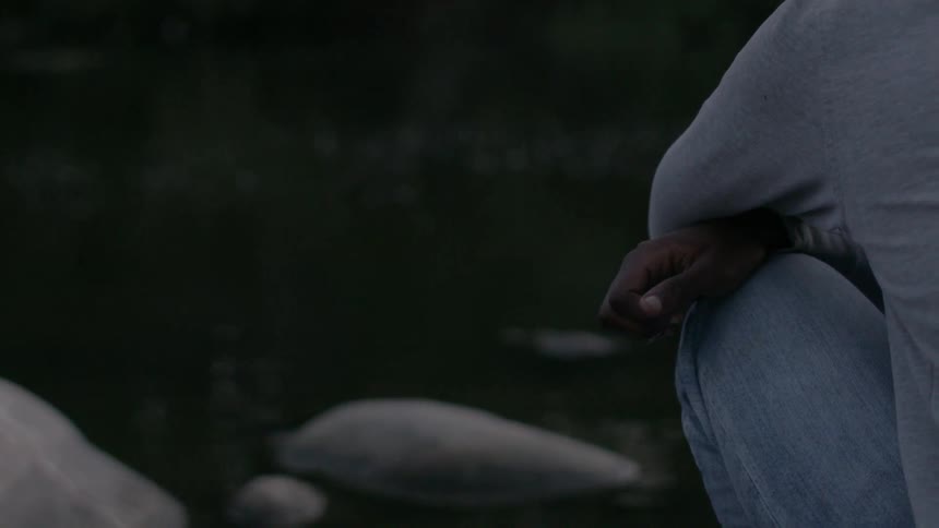 A man kneels next to a river