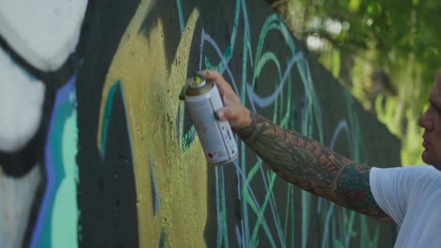 A man spray paints on a concrete wall