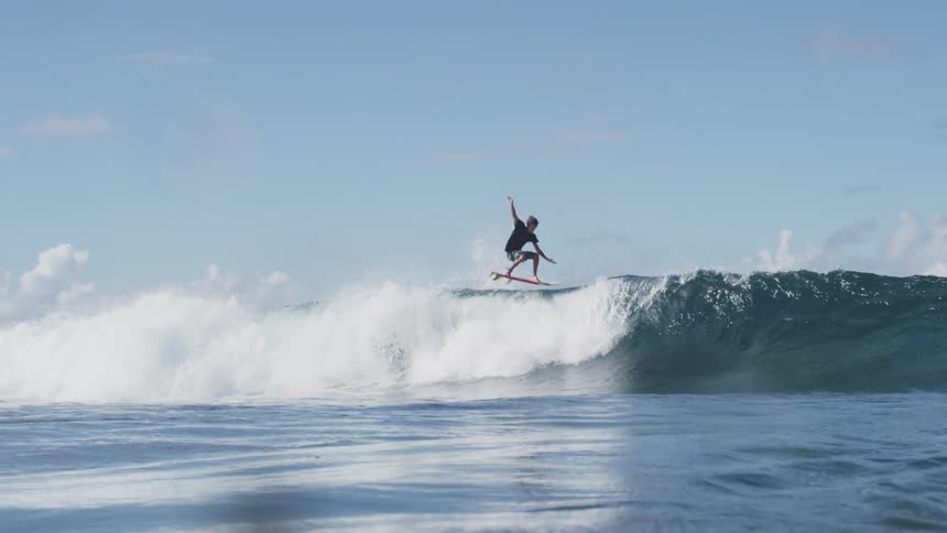 A surfer goes airborne and does a spin in the air while surfing on the ocean during the day