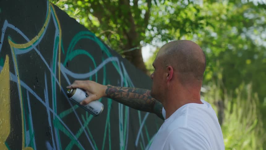 A man is outside and painting a wall using a spray can