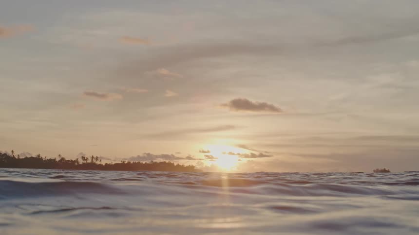 Sun nears horizon as it shines across waves and nearby shore