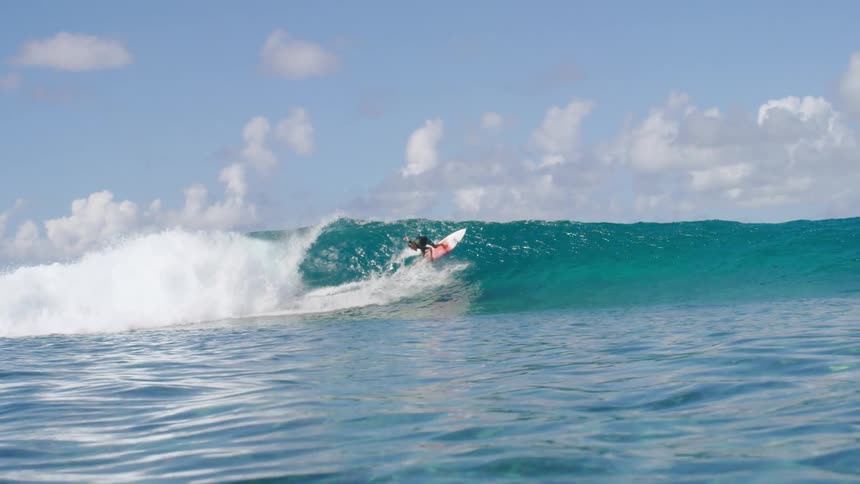 A surfer wearing shorts and a dark colored t shirt rides a wave