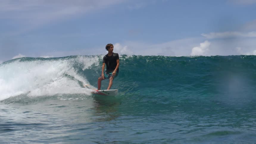 A surfer wearing shorts and a dark colored tshirt rides a wave and wipes out and goes underwater