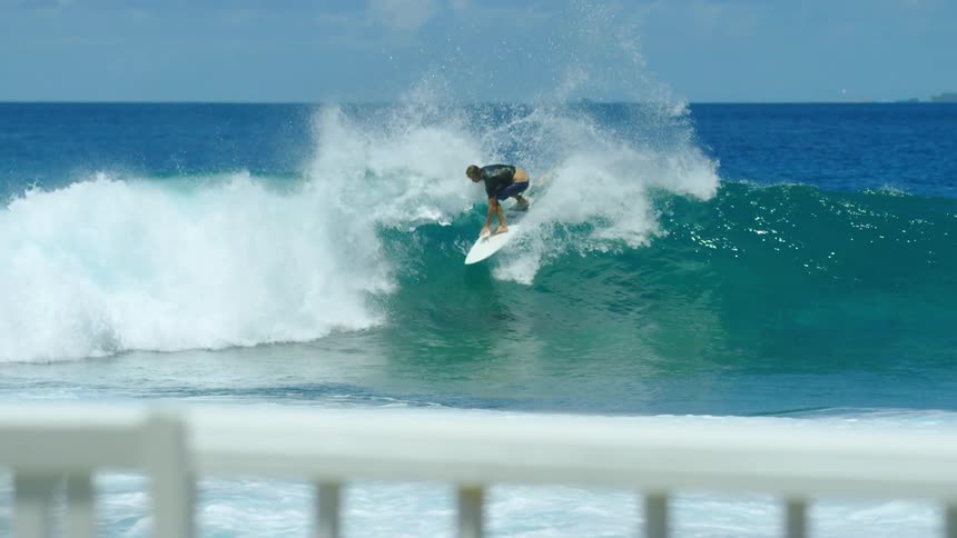 Male surfer with black t shirt and shorts rides ocean wave