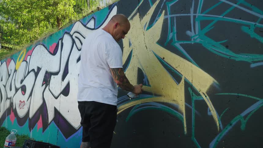 A man is spray painting a wall outdoors in the spring time