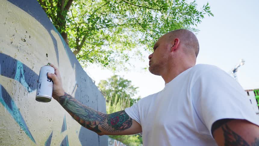 Bald man spray painting a wall near the street