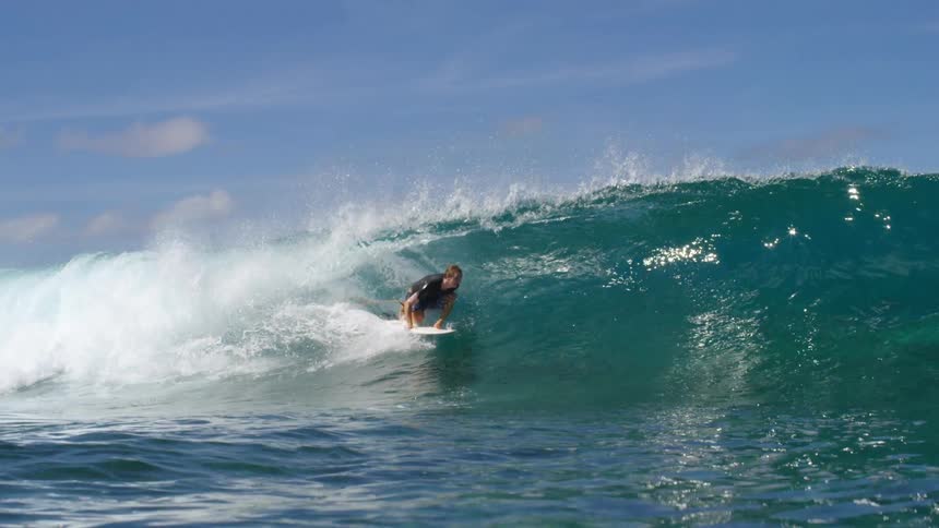 Male surfer with shirt and shorts rides on sea wave