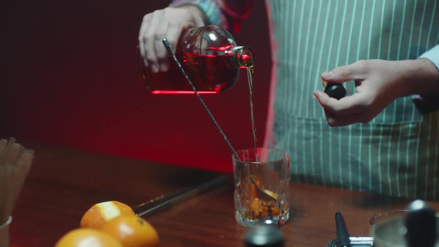 A bartender in a striped apron pouring a drink into a glass