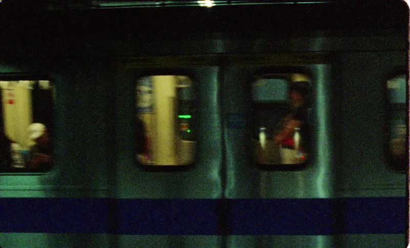 A lighted subway train with people inside travels from right to left