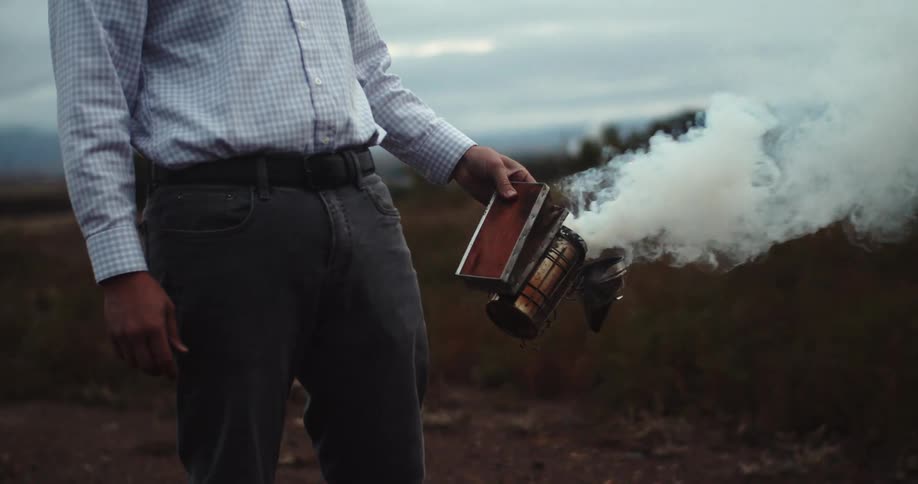 Man manipulates hand held smoke generator while standing outdoors near field