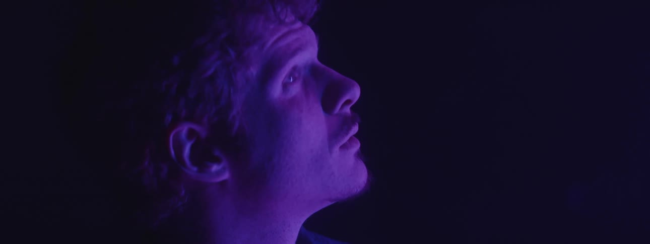 A man looks up as he stands under a black light in a dark room