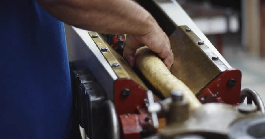 Male worker in factory uses machine to shape tube shaped mass