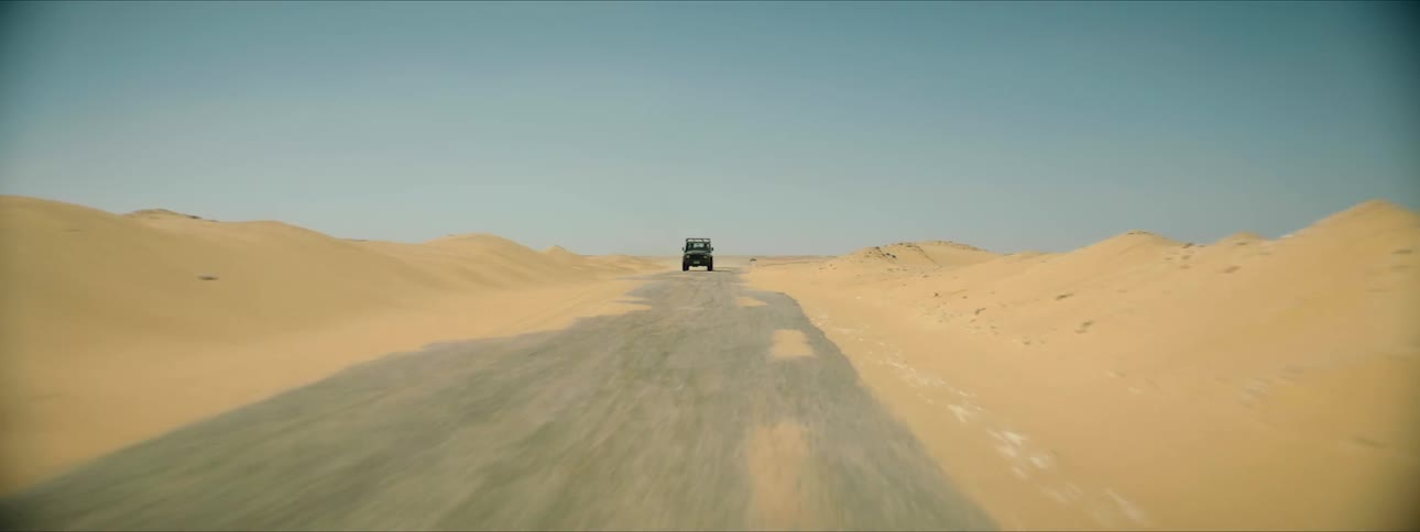 A car is driving through a desert in the daytime