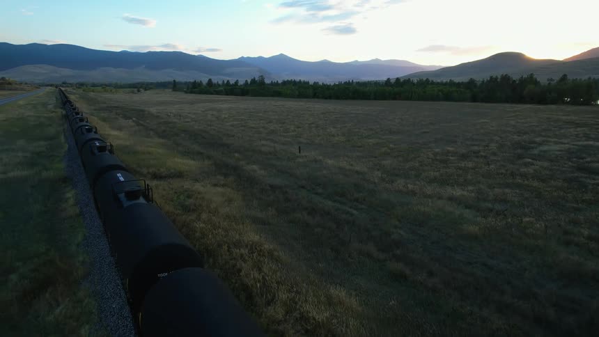 Aerial view of a freight train parked on the tracks in a field near the mountains at morning