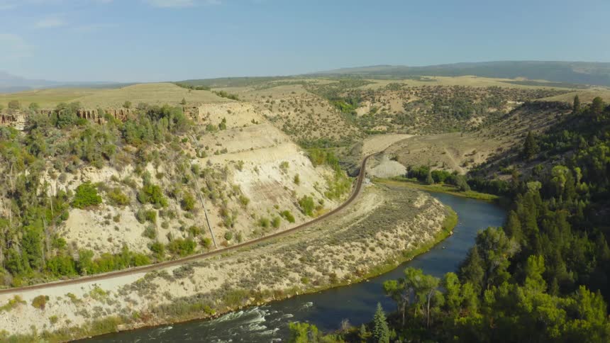 A train track runs alongside a river through a large canyon