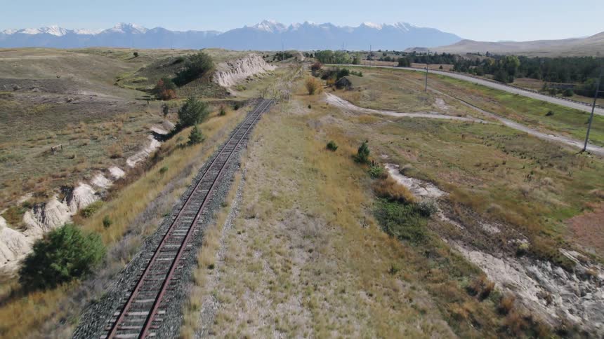 A railroad track that is partially overgrown parallels a roadway through the hills