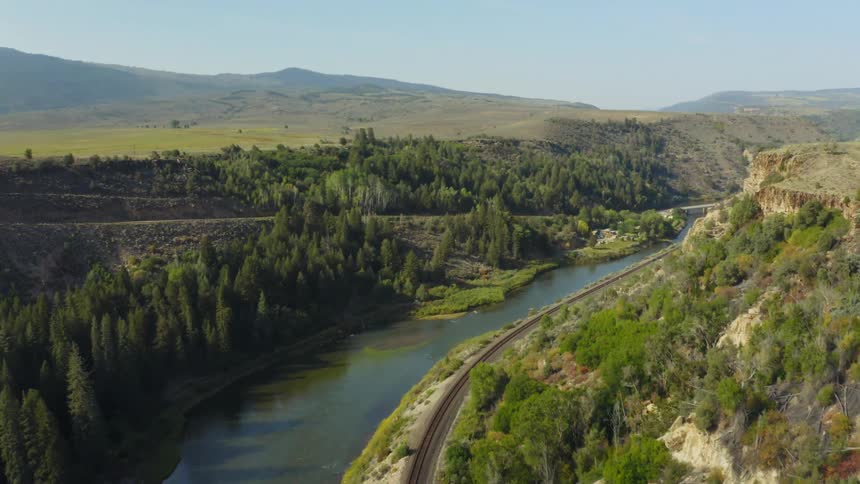 Aerial view of railroad tracks running along a river on a canyon in the morning