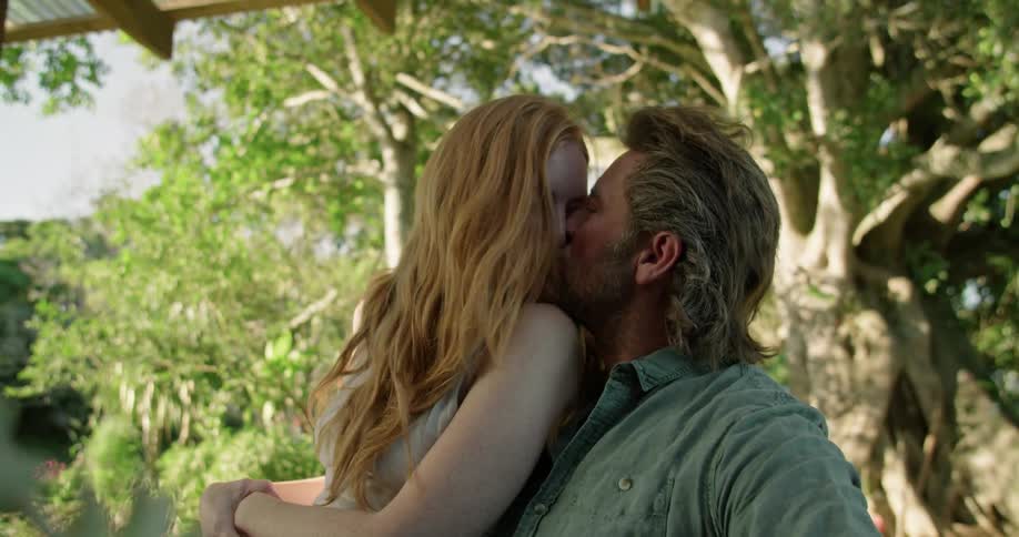 Couple sitting under large tree smiling and kissing