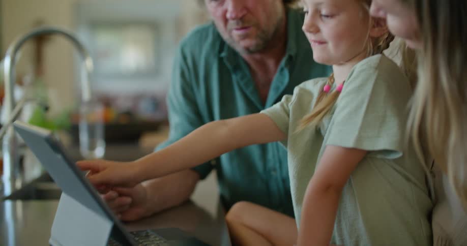 Middle aged father blonde mother and daughter use tablet on kitchen counter in the kitchen