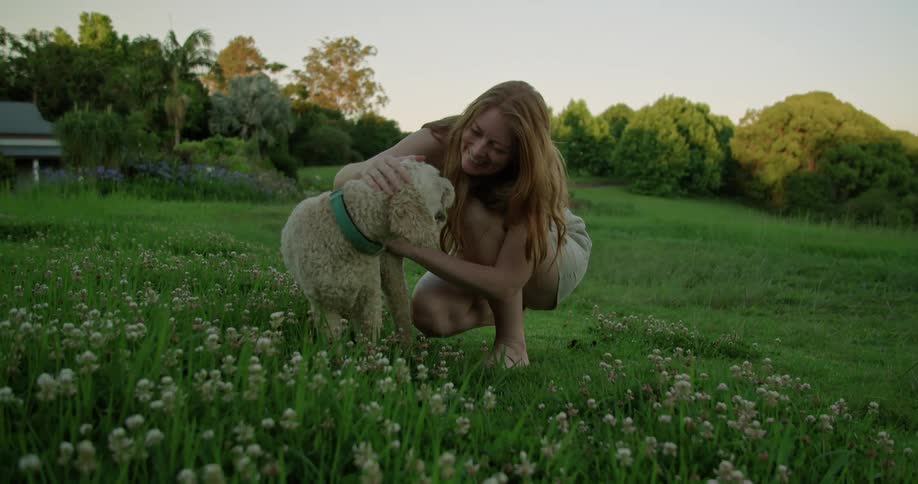Woman crouches in shadowed yard petting a dog and smiling