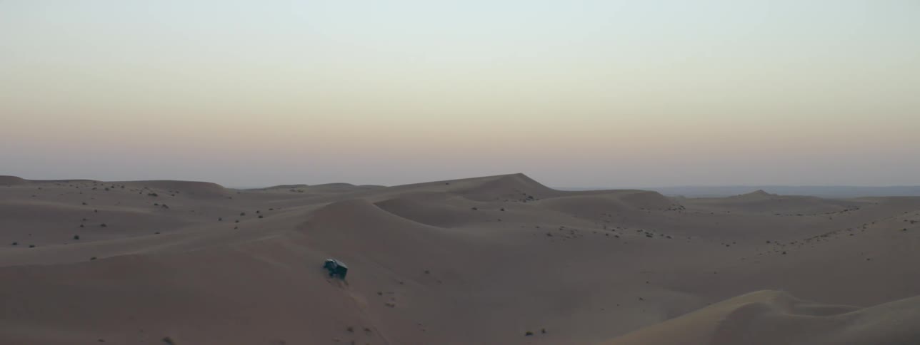 Jeep drives up and down slope in desert under a red tinted sky