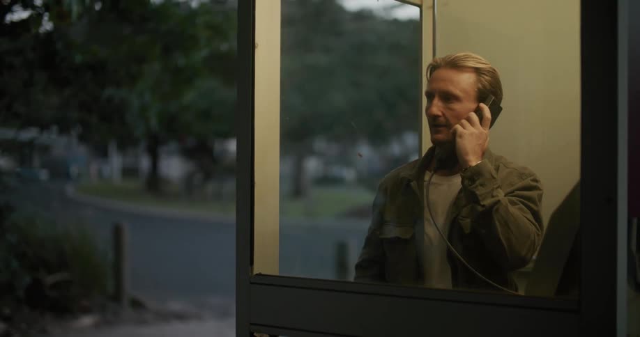 A man is talking on the telephone and he takes off his black cap and puts it back on his head as he is talking