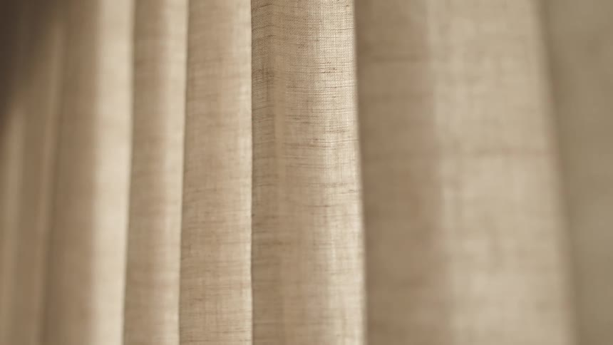 Sunlight shines through a drawn beige curtain