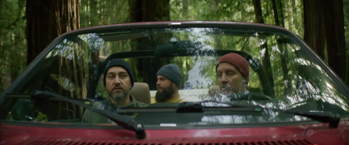Three men drive in a car through the forest