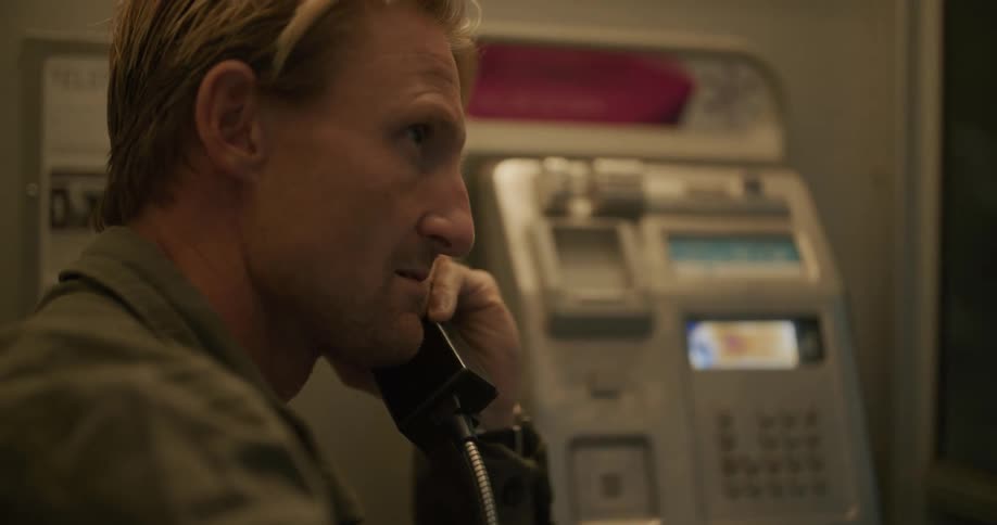 A man is talking on a telephone in a phone booth