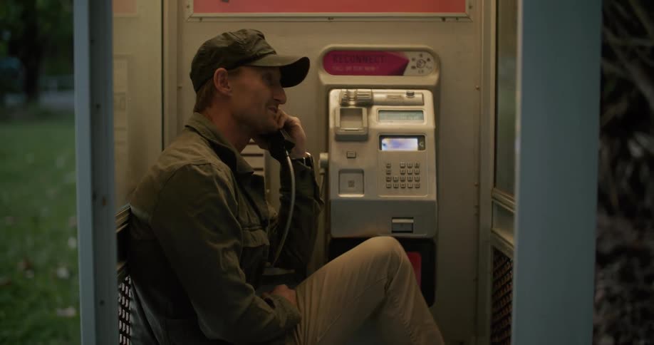 Man sitting inside a phone boot talking on a payphone outdoors