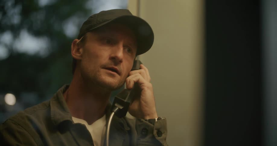 A man is standing indoors and talking on a telephone