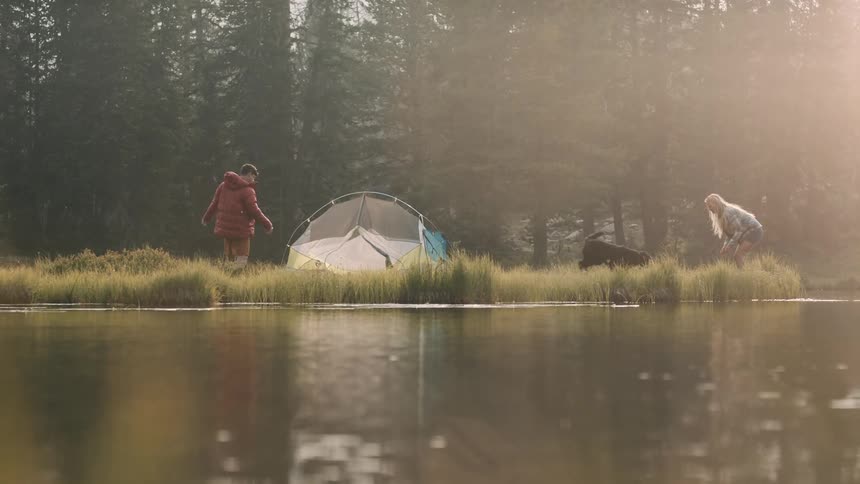 A couple playing with their dog at their campsite by the lake