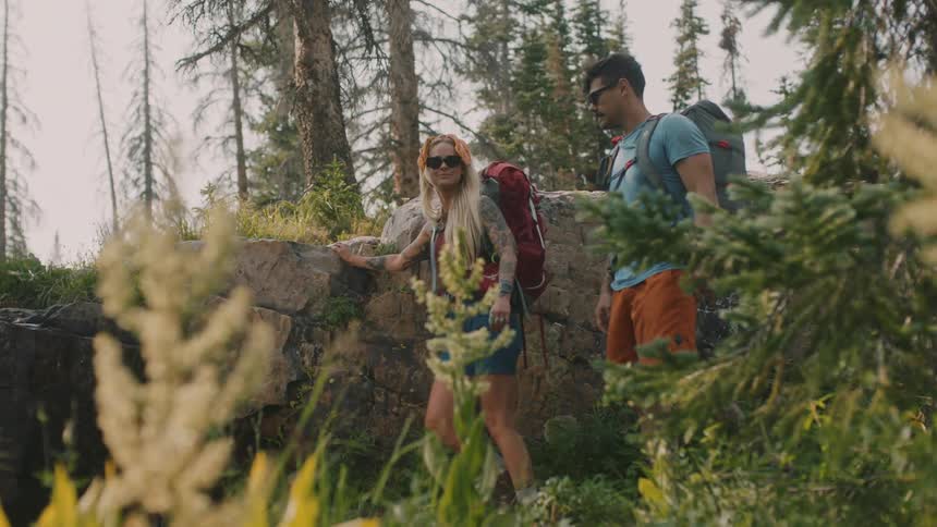 Young couple carrying backpacks hiking near a stream in the forest