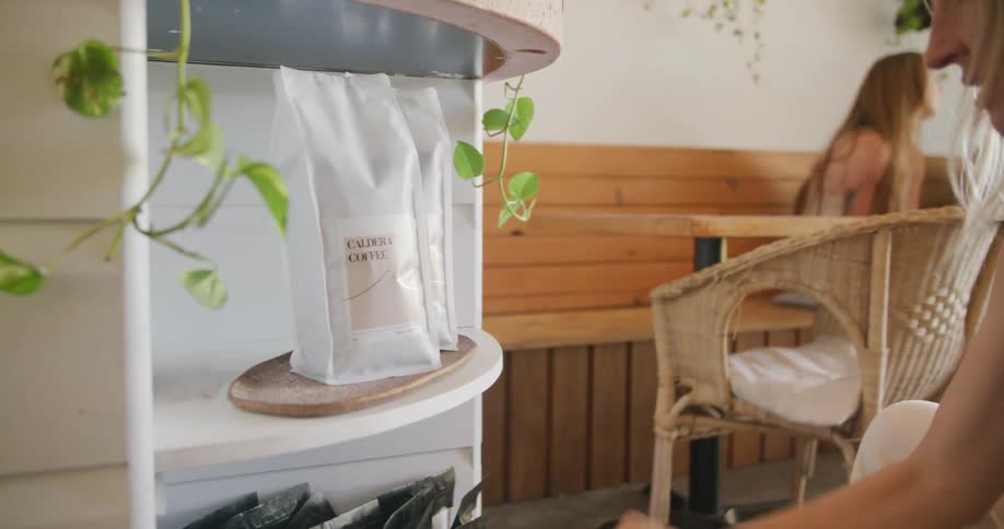 Young blonde woman organizing coffee bags on a shelf inside a restaurant