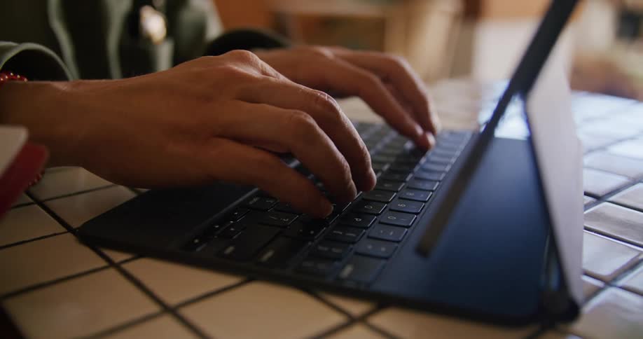 Man with green jacket types on tablet keyboard in cafe