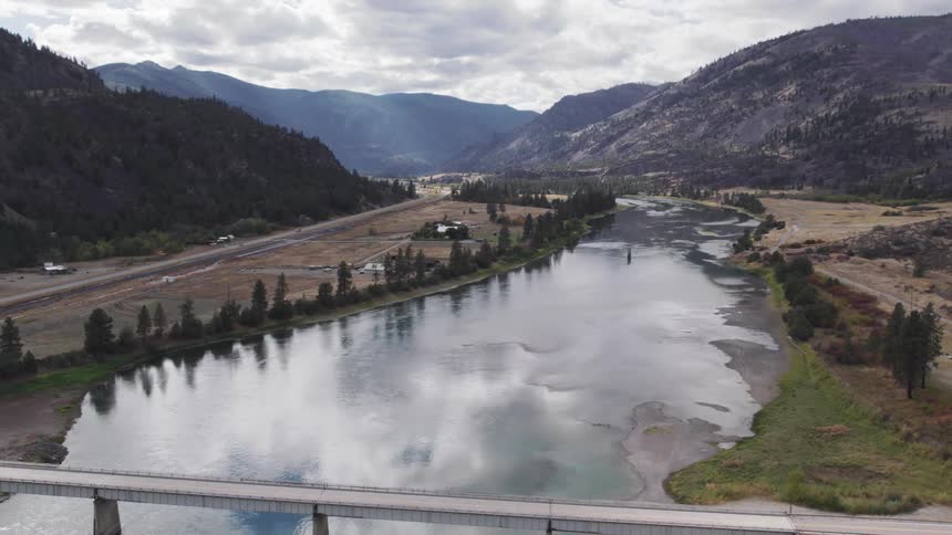 A peaceful river flows through a valley under a cloudy sky
