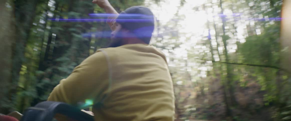 Man standing on the back of a car while driving on a road through the forest