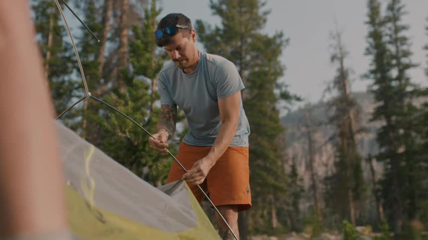 A man is setting up a tent by the forest