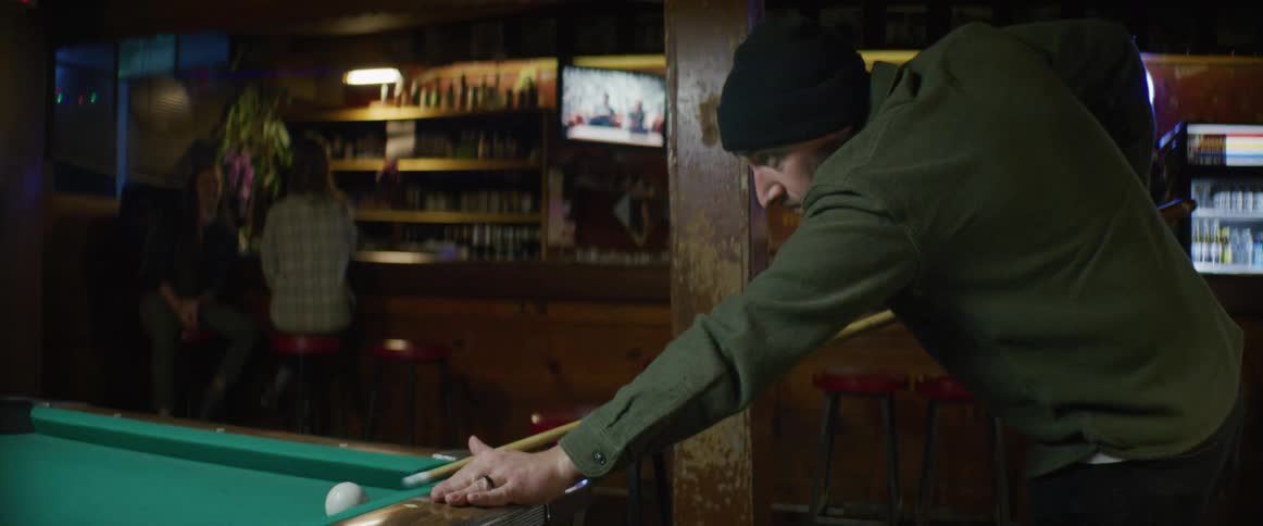 Man wearing a black beanie playing pool inside a bar